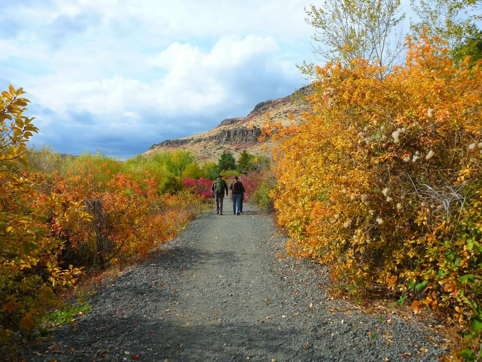 Three hikers on a flat gravel hiking trail with fall colors and rocks around them