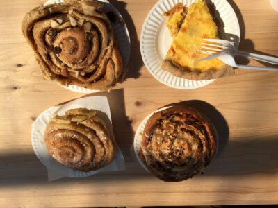 Three cinnamon rolls and a slice of quiche on paper plates on a wooden table