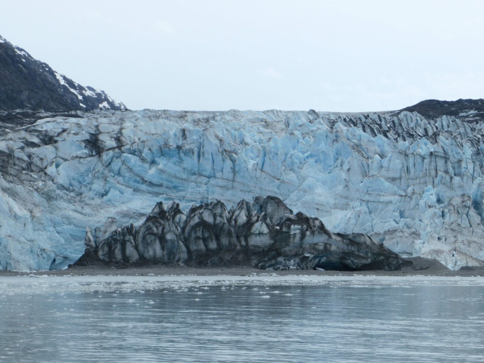 A blue tidewater glacier between mountains and rocks on an overcast day is a highlight of the best alaska cruise ports