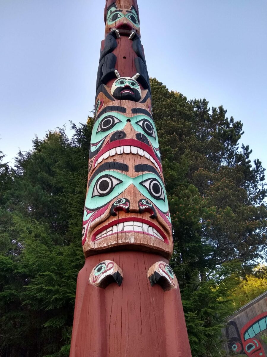 A totem pole in red and turquoise paint in a forest on an alaska cruise excursion in ketchikan at Saxman Native Village