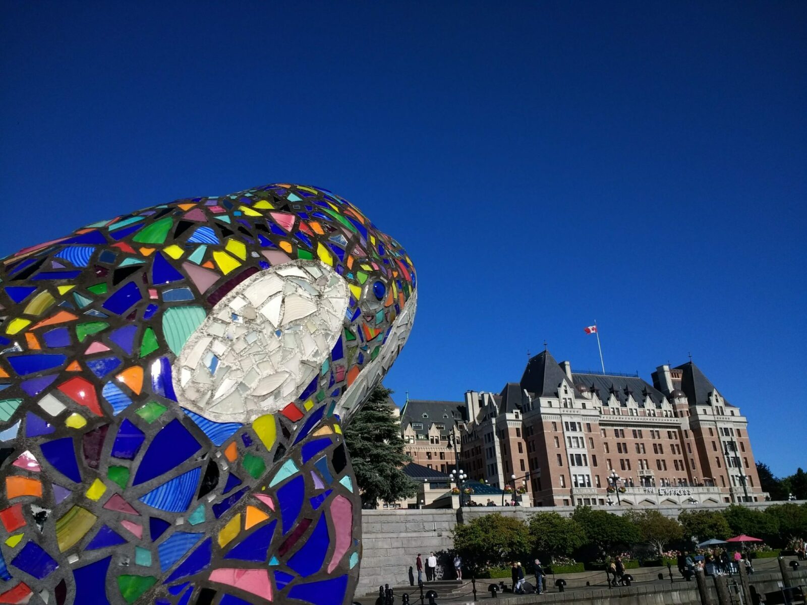 A colorful orca sculpture is in the foreground and a large stone hotel in the background. It's a blue sky day.