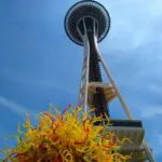 The Space Needle against the blue sky with a yellow glass sculpture in the foreground.