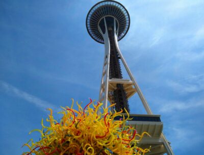The Space Needle against the blue sky with a yellow glass sculpture in the foreground.