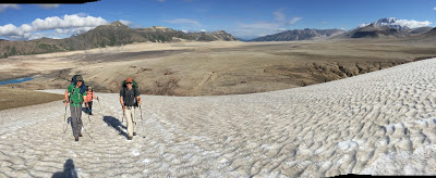 Three hikers walking up a field of snow in Katmai National Park. In the background is a valley and many mountains