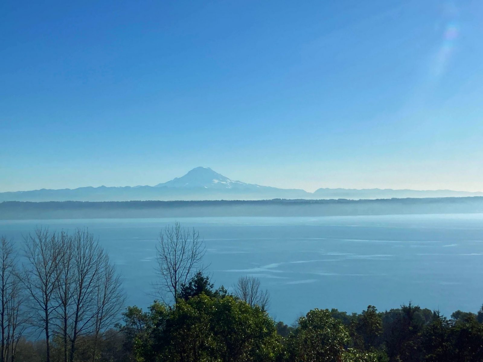 A high mountain above forested hills seen across a body of water with forest in the foreground