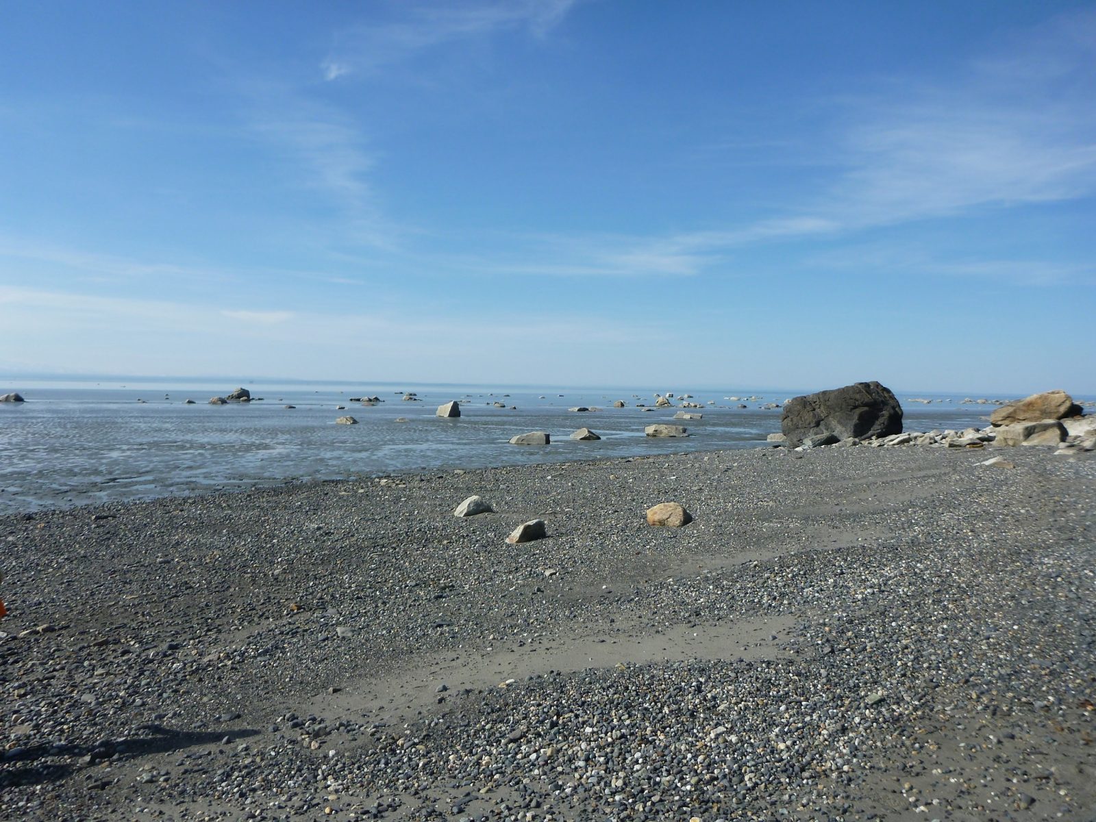 A gravel beach with large rocks at low tide on a sunny day