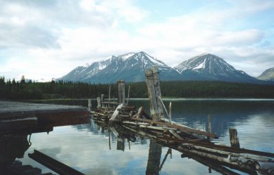 Mountains with lingering snow are seen across a lake. The lake is surrounded by forest