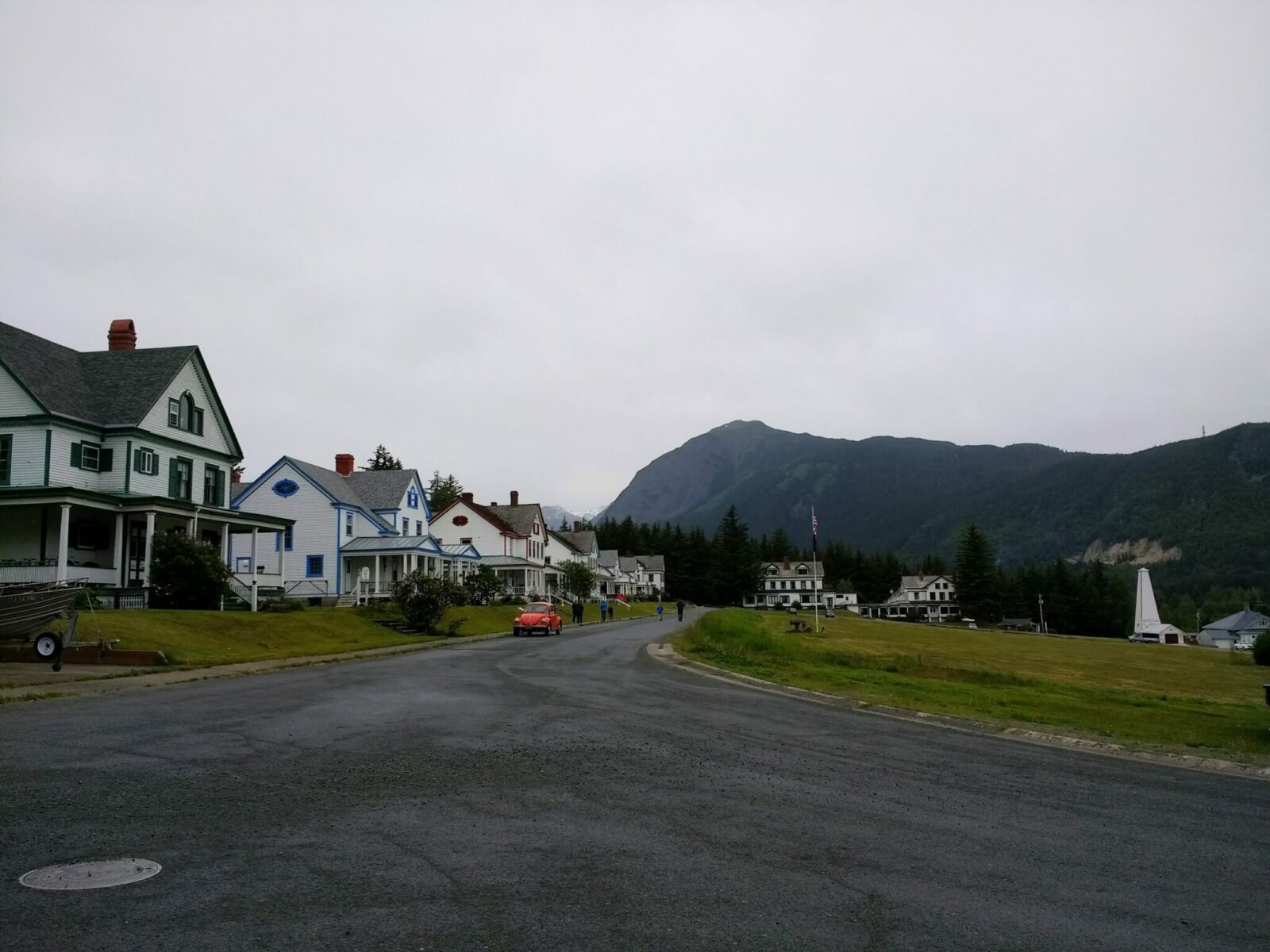 Historic Fort Seward in Haines, Alaska. There is a paved road going by historic army officers housing and a large parade green on the other side of the road. Mountains are in the distance