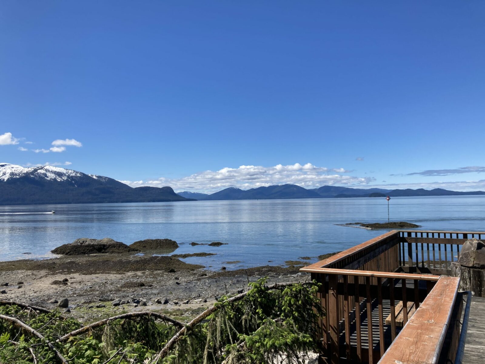 A wooden boardwalk with railings above a rocky beach. Across the water are forested mountains