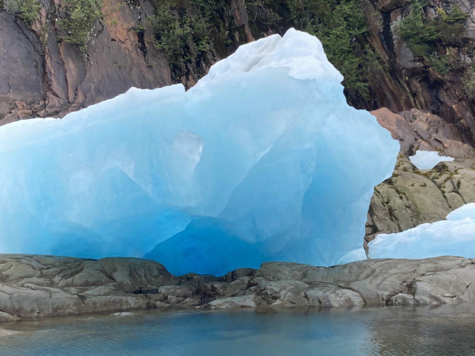 A large, bright blue iceberg about the size of a garage sits on the rocks near LeConte Glacier