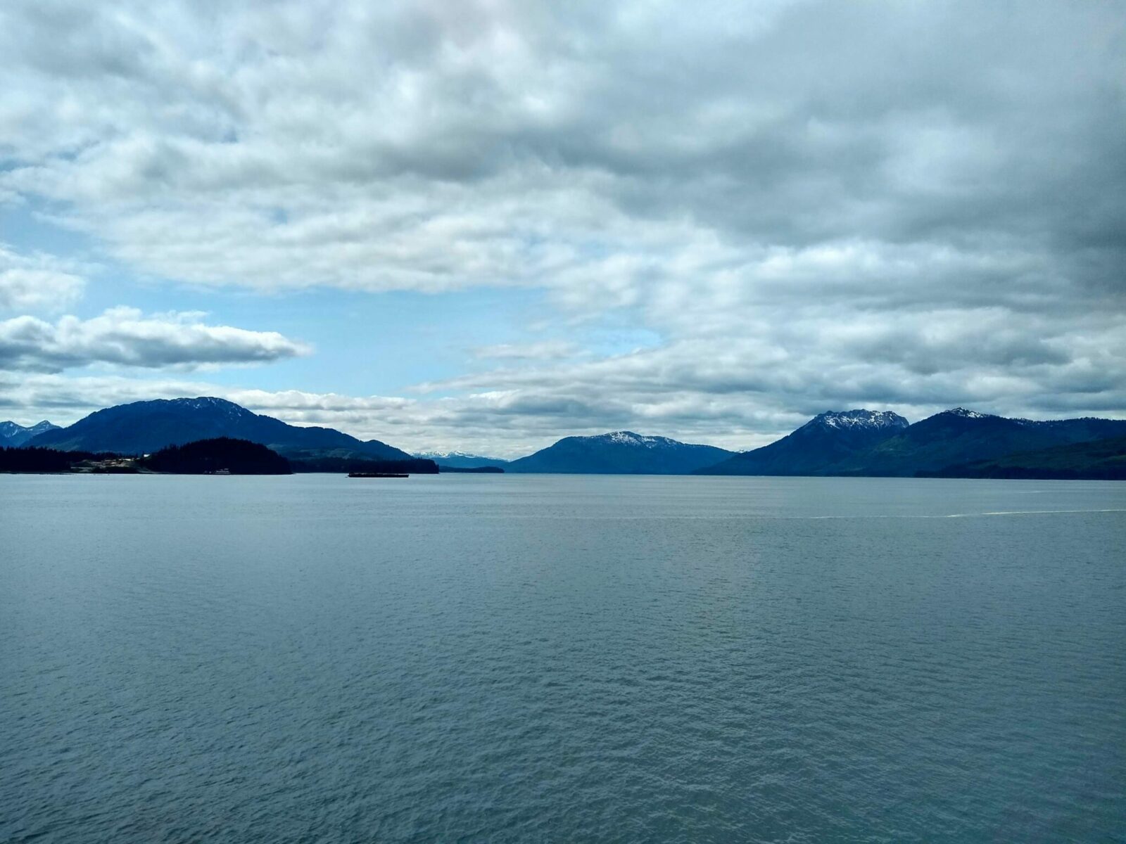 Gray ocean and dark mountains surrounding it on a mostly cloudy day near Icy Strait Point, one of the best alaska cruise ports