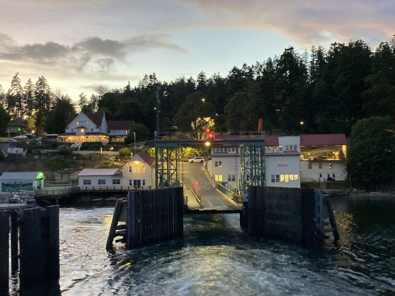 a ferry terminal on orcas island. there is a ramp and white buildings with red roofs on each side. It's getting dark and the buildings are surrounded by forest