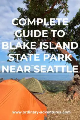 A madrona tree near the beach with water and forested land in the distance. Under the tree are two tents, one orange and one green. Text reads: complete guide to Blake Island State Park near Seattle