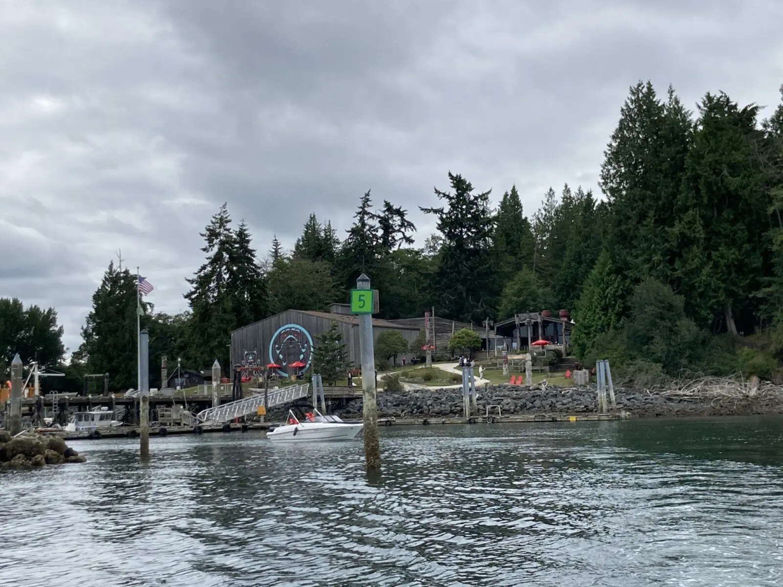 The entrance to a small marina in the forest on Blake Island. There is a building with Northwest Coast art painted on the side facing the marina