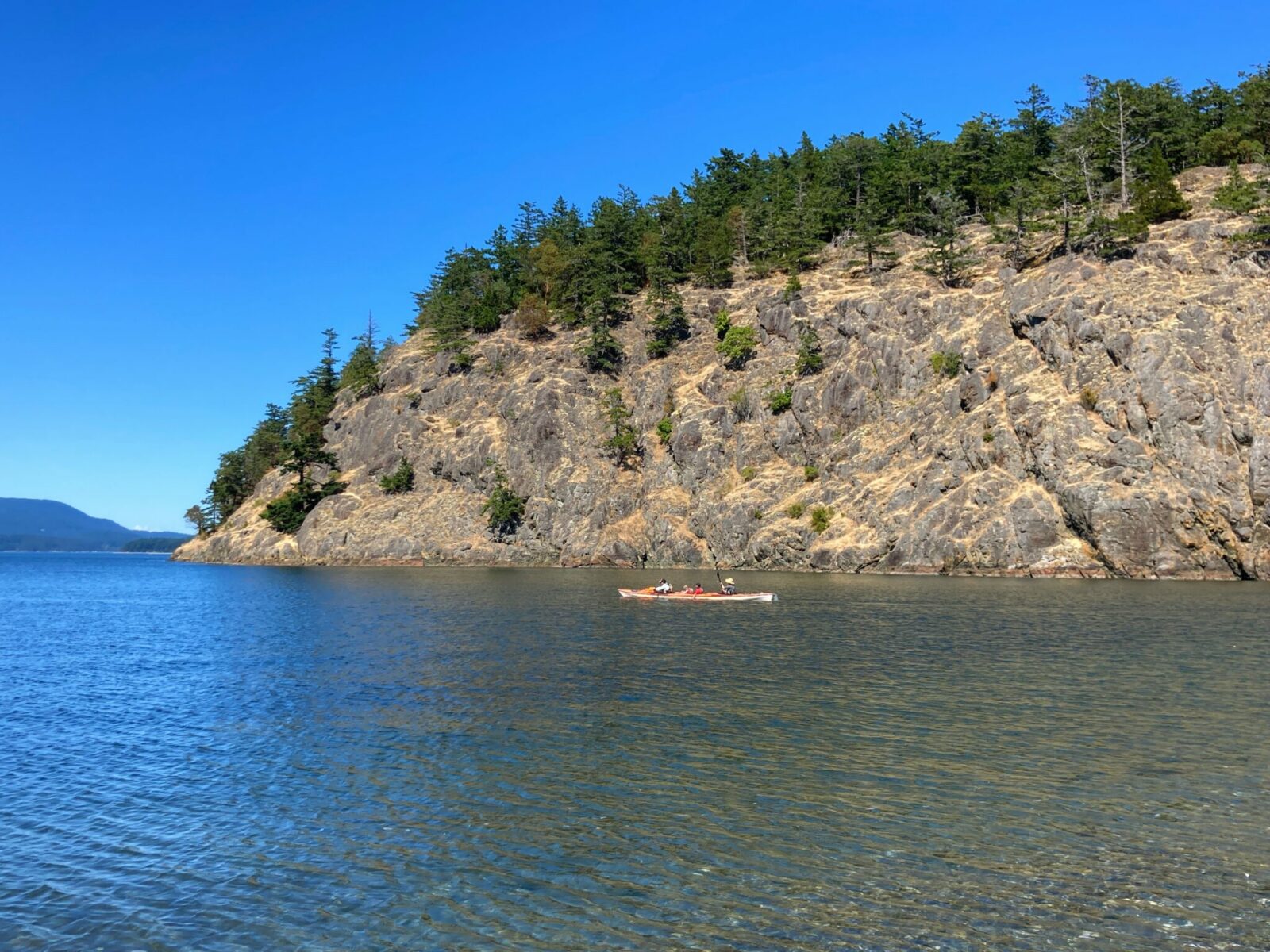 Kayaking is a wonderful thing to do on Lopez Island. A trip kayak is in calm water between the beach and a nearby rocky and tree covered island