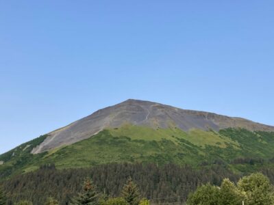 a rocky pointed mountain summit rising up from the forest below. A trail is visible on the side of the mountain.