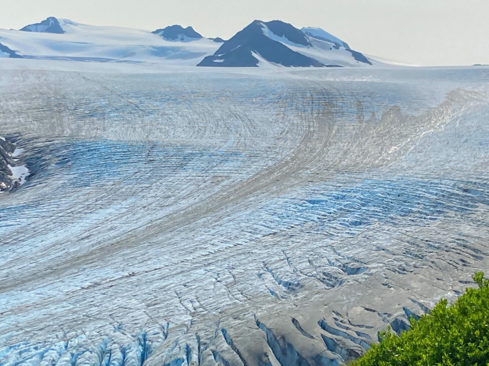 A glacier of Blue ice with crevaces and higher glaciated mountains in the distance