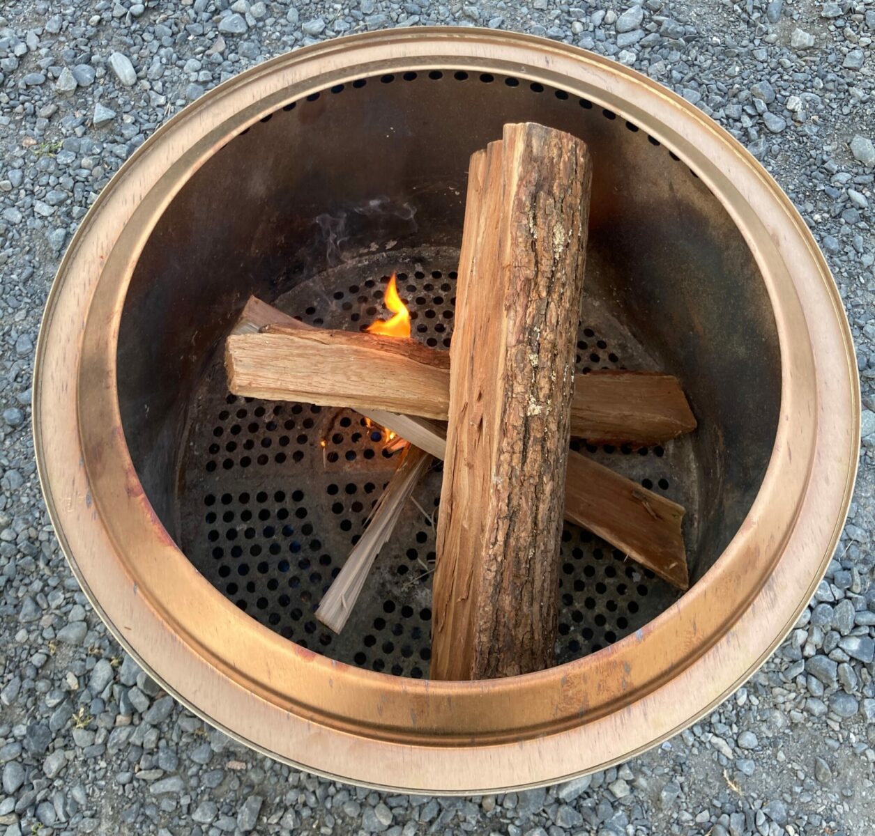 Four pieces of wood in a top down view of a smokeless fire pit. There is a small flame just starting to light the fire.