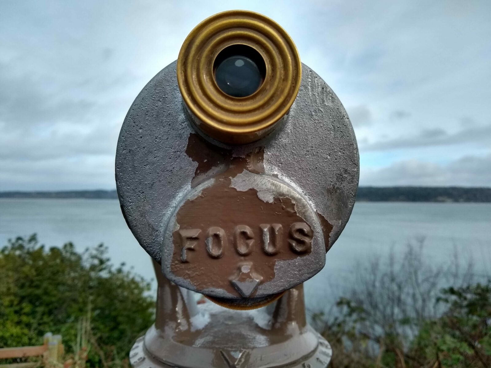 An old spotting scope that says "focus" near a bluff overlooking the water