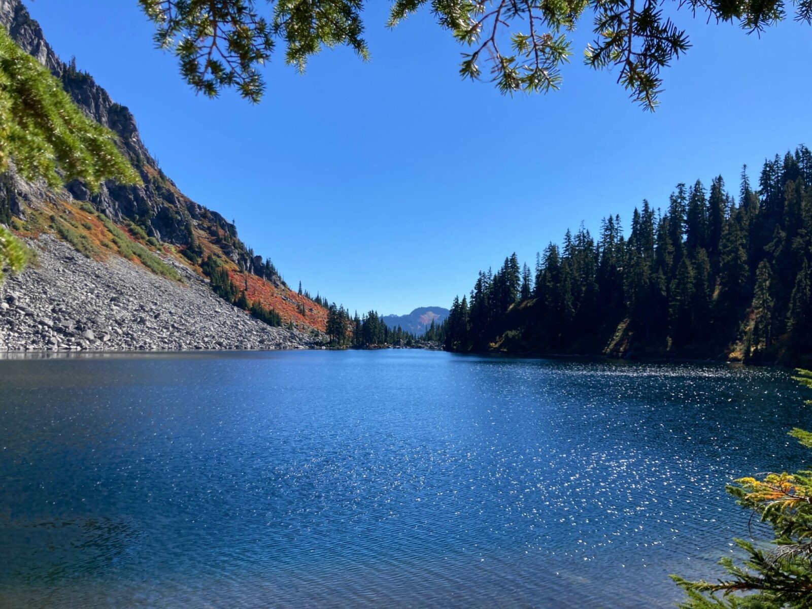 Lake Valhalla on a sunny day, surrounded by evergreen trees and gray rocks.