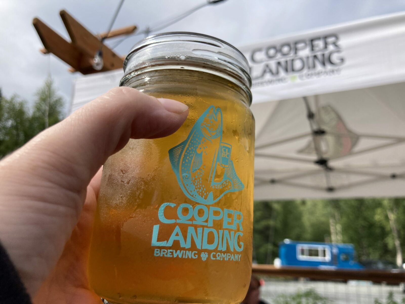 a glass jar with beer in it that says "cooper landing brewing company" with a picture of a salmon. A person's hand is holding the beer