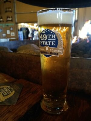 A glass of beer on a bar. The glass says 49th State brewing company, Anchorage Alaska, one of the breweries in Alaska