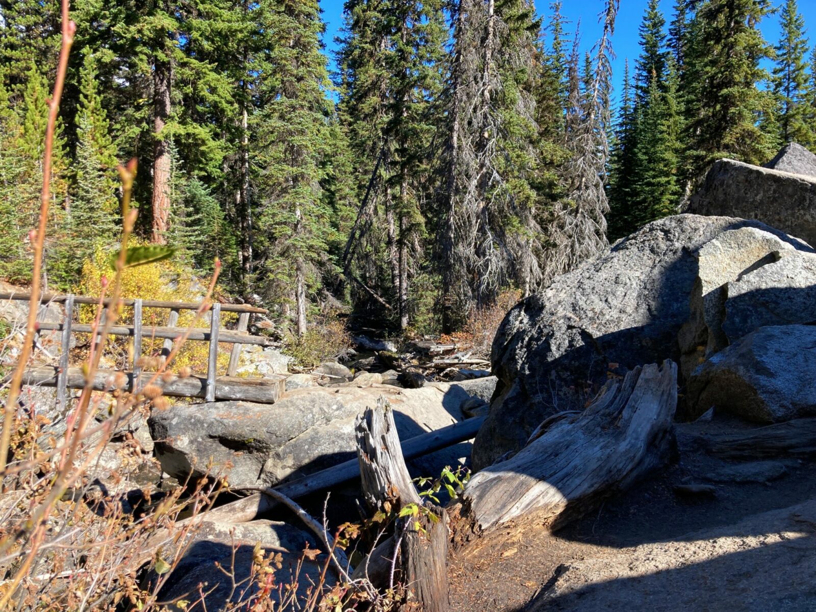 A jumble of boulders in the forest next to a wooden bridge over a creek