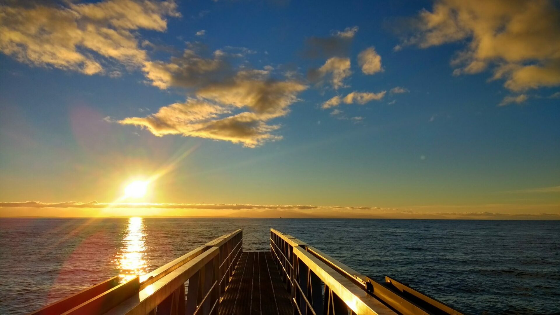 The sun setting over the water with a metal pier in the foreground