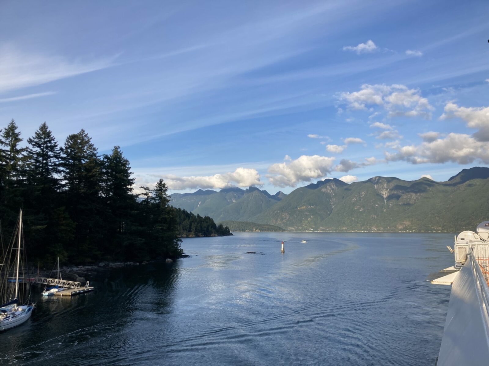 The side of a ferry in a small cove surrounded by forests across the water from forested mountains