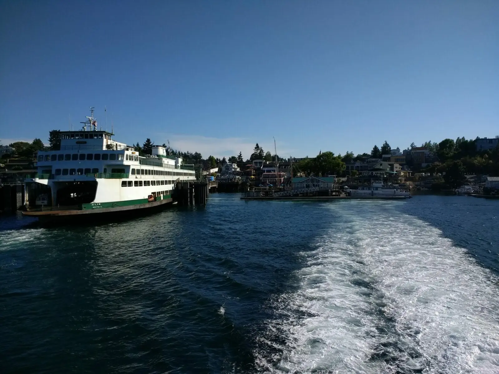 The ferry approaching the dock in the small town of Friday Harbor Washington, one of the best things to do on san juan island. There are trees surrounding the buildings and docks.