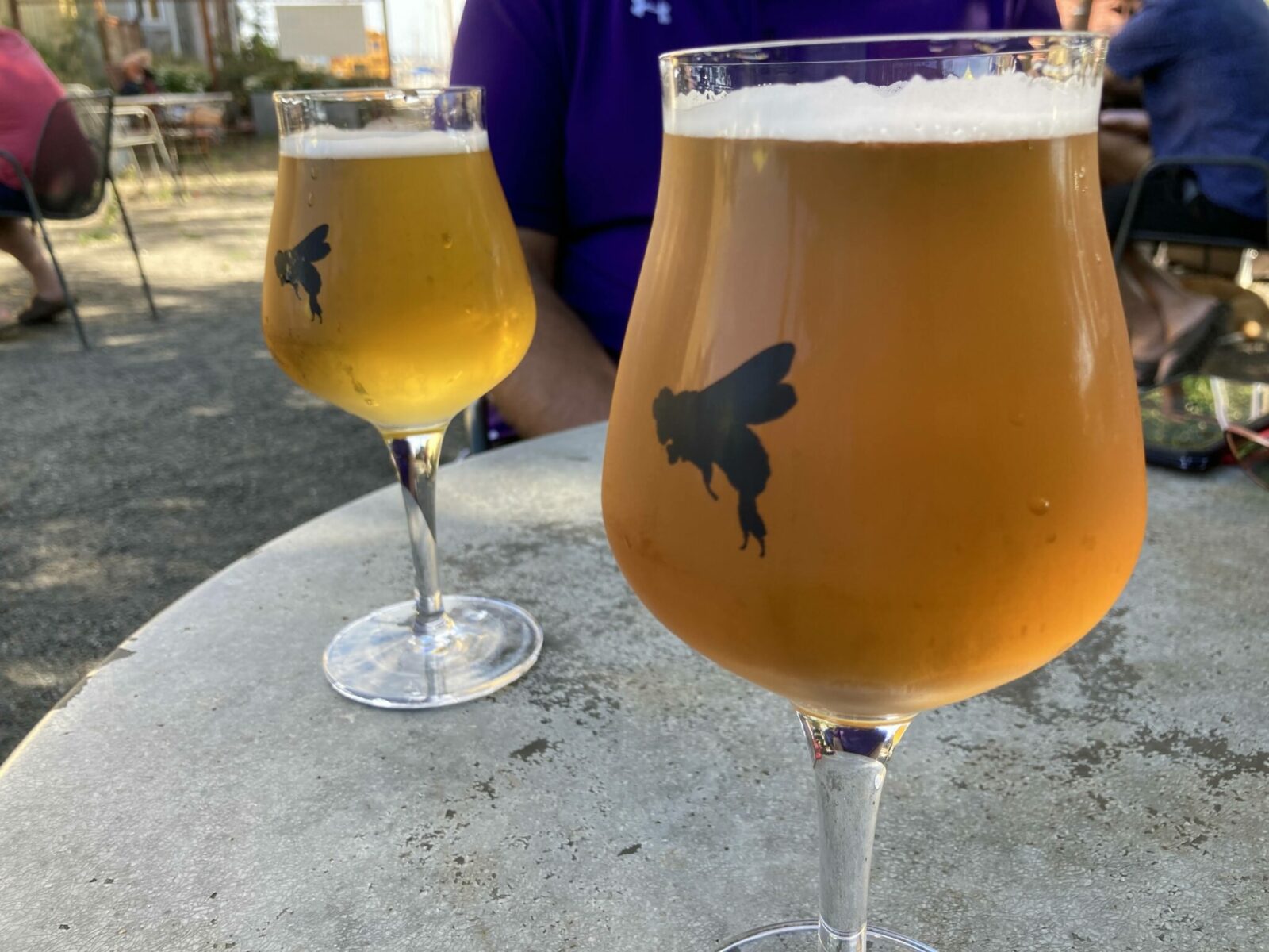 Two goblets filled with light beer on a concrete table. Each goblet has a chrysalis painted on it in black.