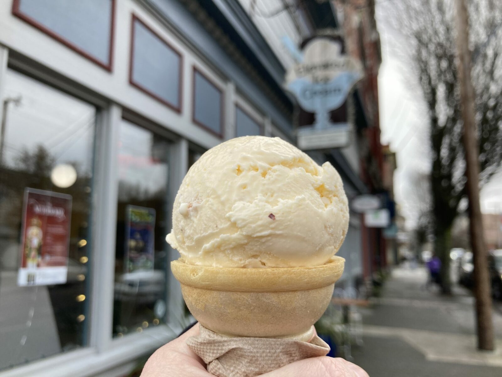 A person's hand holding an ice cream cone on a city street