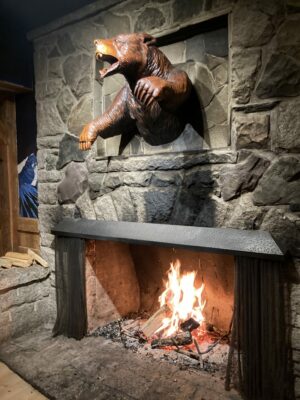 A fireplace with a wood fire and a stone chimney with a wooden carved bear