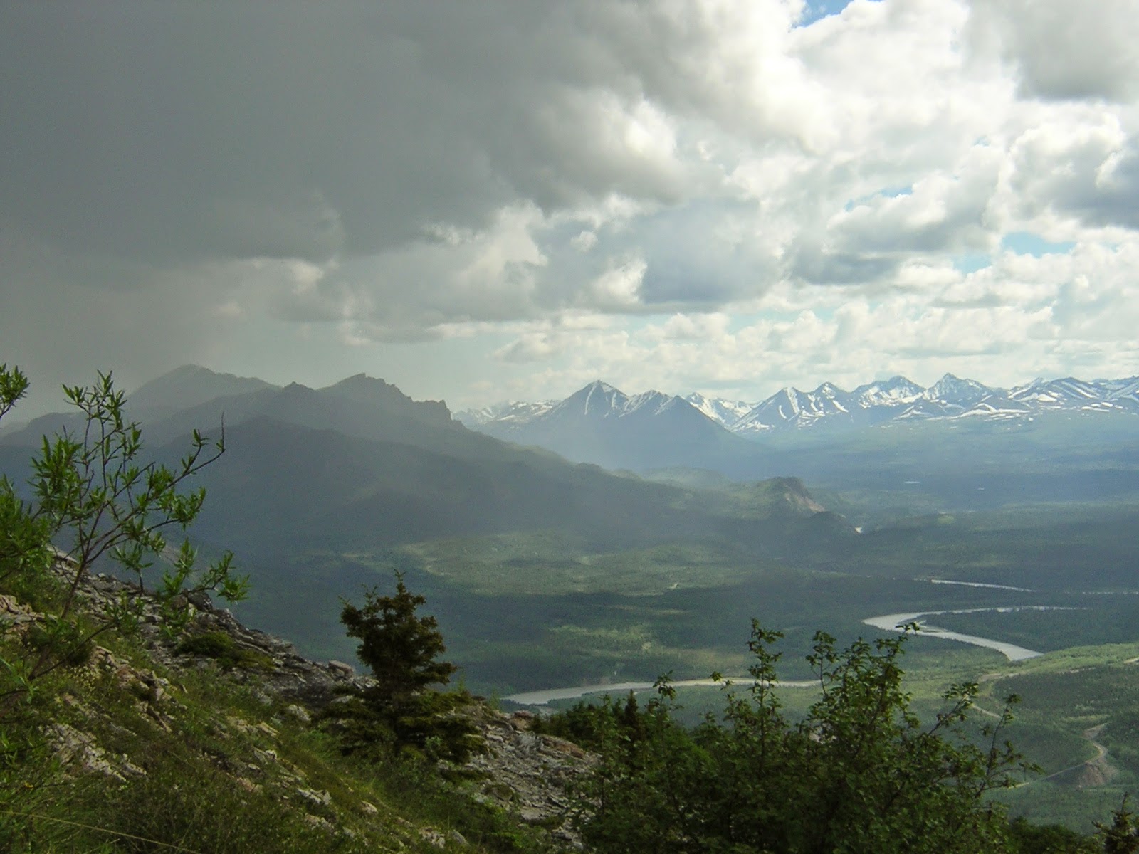 A view from a ridge on a cloudy with good visibility down to a river valley with distant mountains across the valley