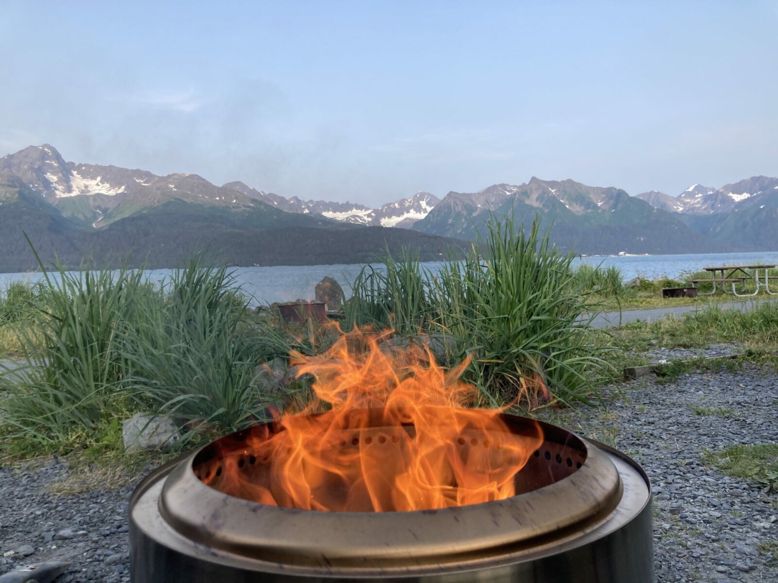 a firepit with a fire near the shore with mountains in the distance camping in alaska in seward.