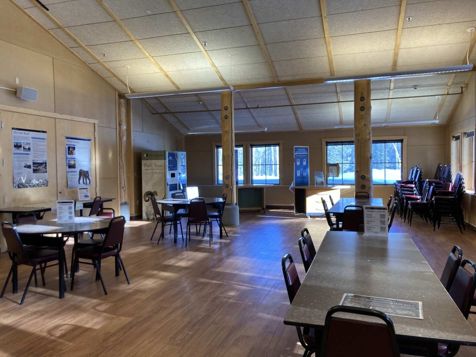 The interior of a building in Denali National Park in winter. There are informational posters about the park on the walls and there are tables and chairs for people to eat lunch at