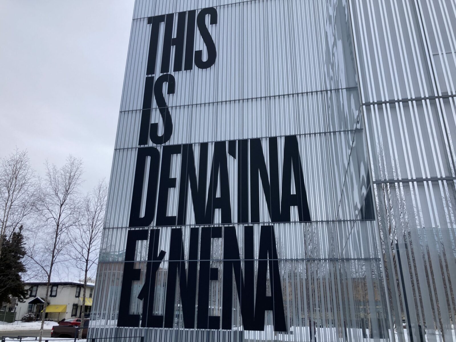 A glass building with large black letters reading This is Dena'ina Elnena.