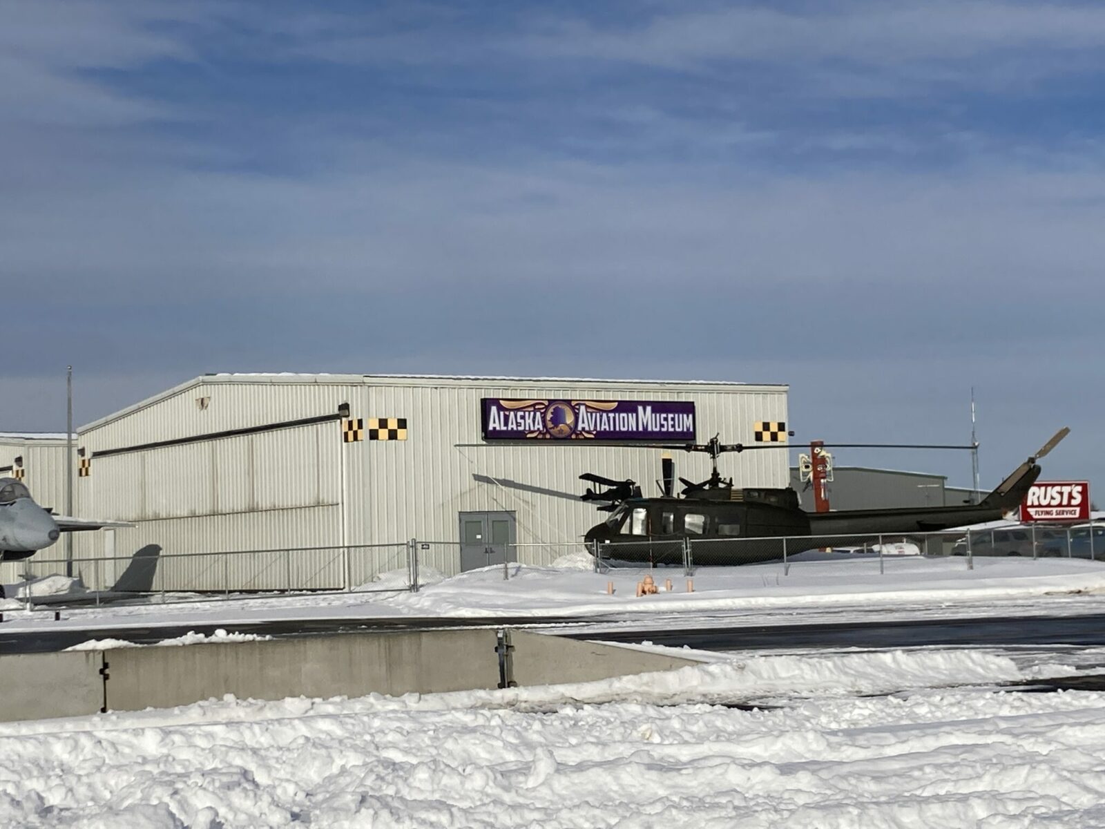 A hanger with a helicopter in front and a sign that reads Alaska Aviation Museum