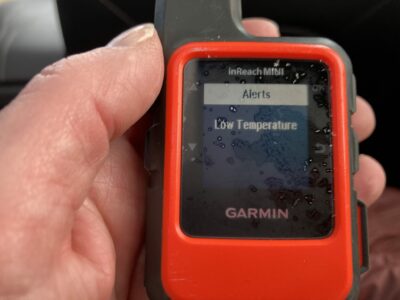 A garmin in reach mini displaying a low temperature alert. It is bright orange and being held in someone's hand