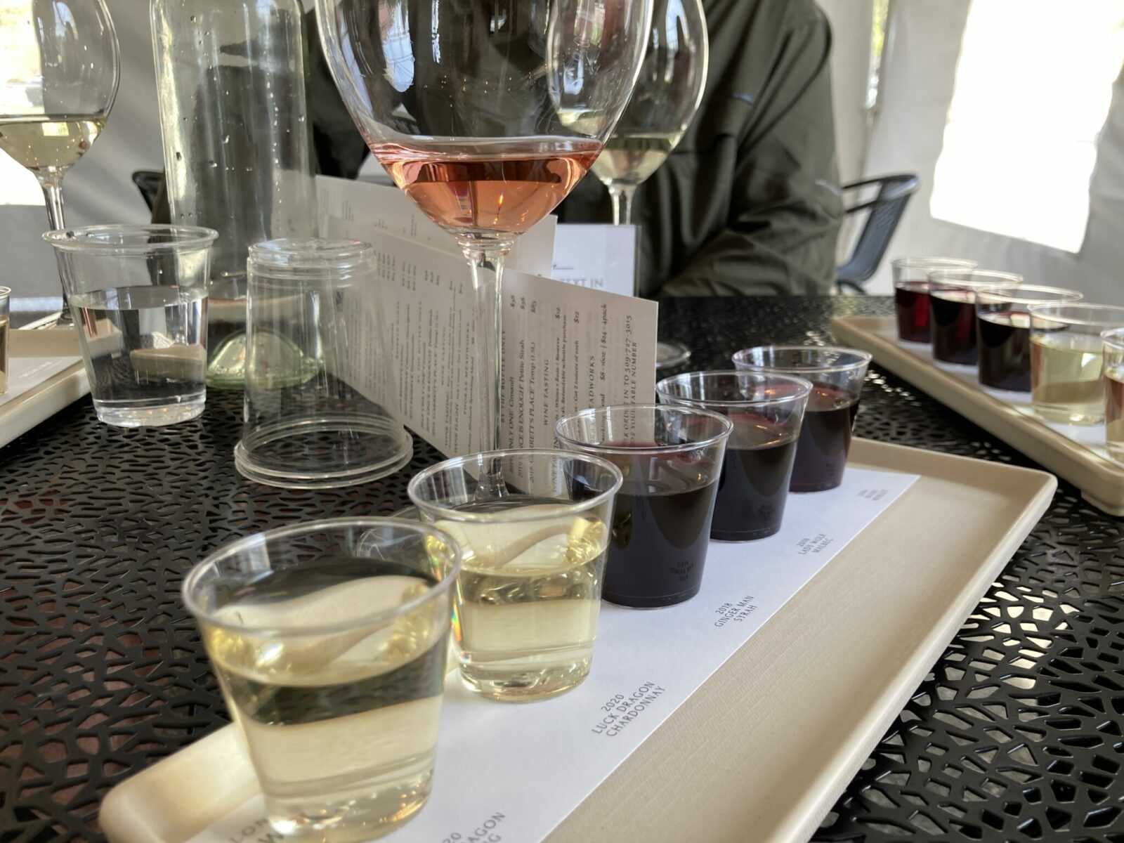 Five tastes of wine (two whites and one red) on a tray on a table with a glass of rose beside them