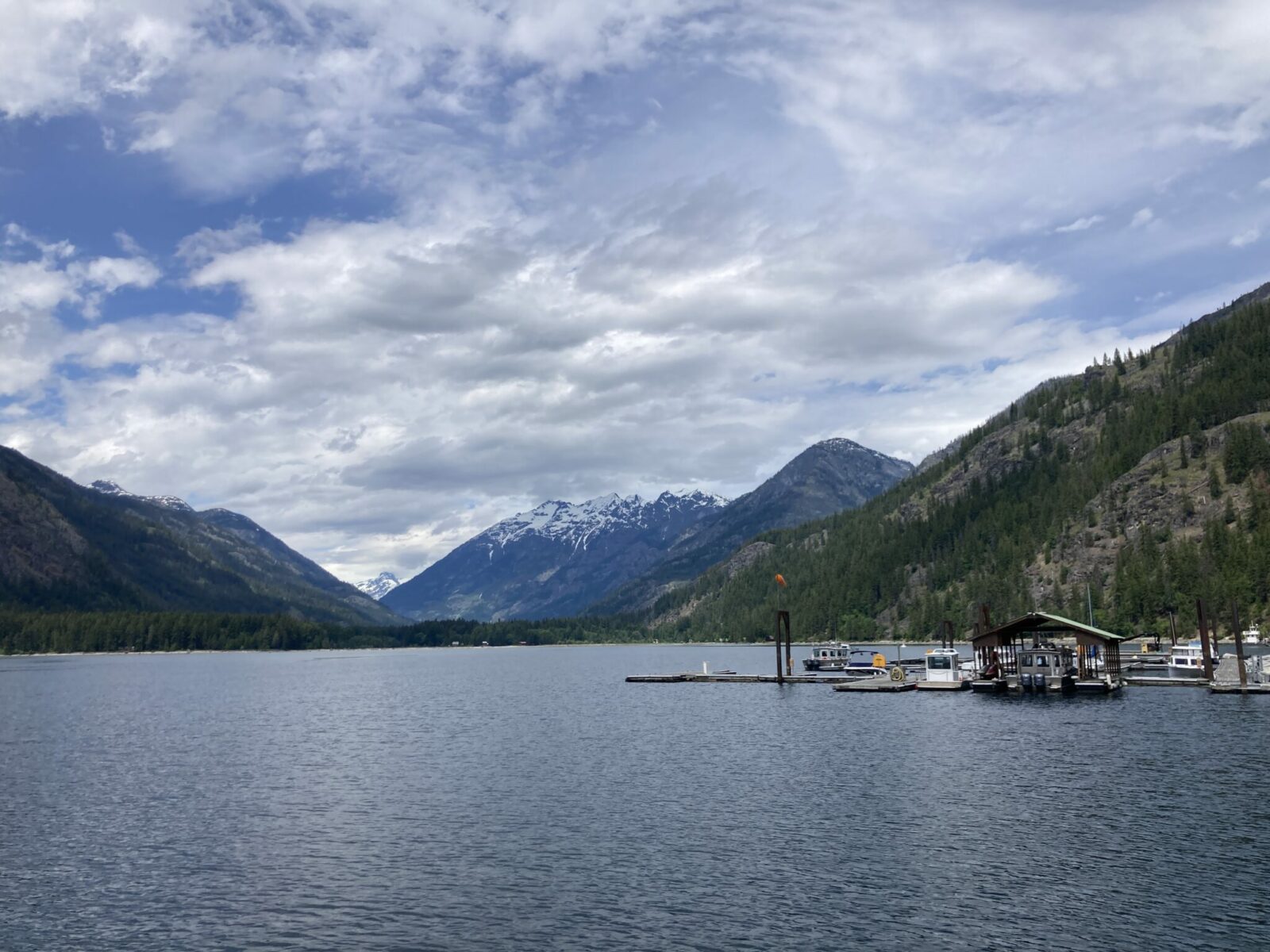 The Stehekin ferry landing at the head of Lake Chelan. A few boats are moored and the lake is surrounded by forested hills and snow capped mountains on a cloudy day