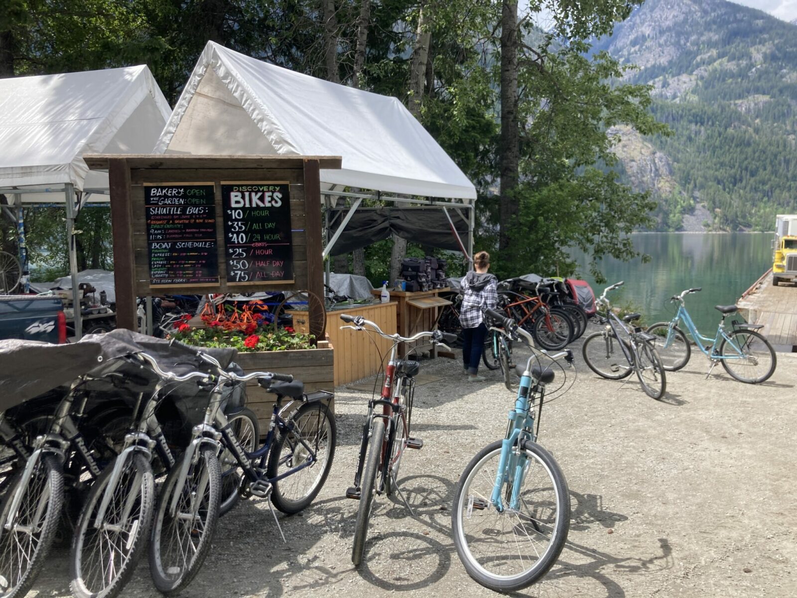 Bikes for rent next to a lake and near a white tent with a sign showing prices