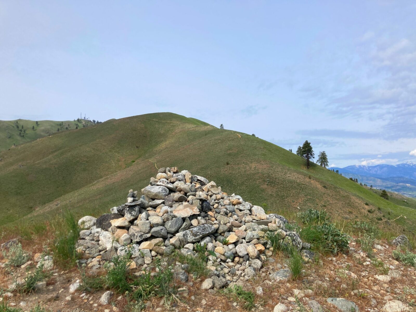 A pile of rocks marking the top of Elephant Head on the Chelan Butte Trail near Lake Chelan. A higher green mountain is behind it and some mountains in the distance