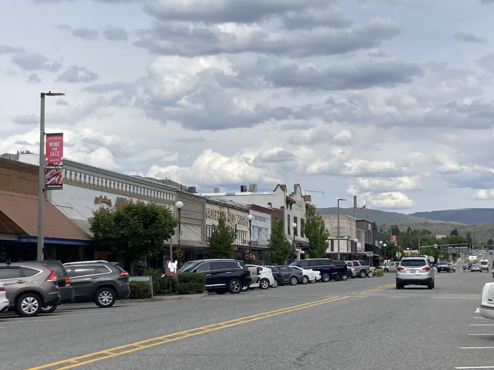 The main street of a historic town. There are cars parked on both sides and many businesses