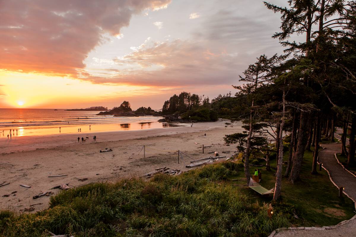 A sunset over a sandy beach with trees and a boardwalk next to the beach near Ucluelet and Tofino.