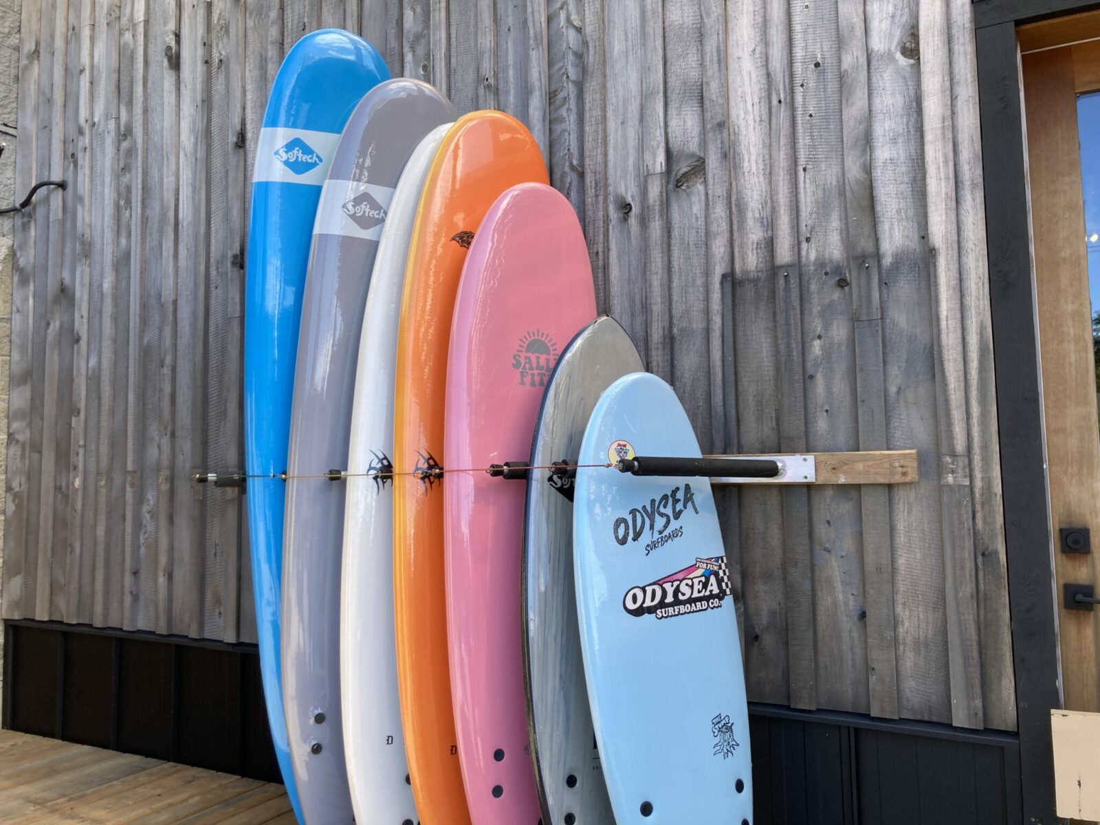 Seven Surfboards in different colors standing up next to a building.