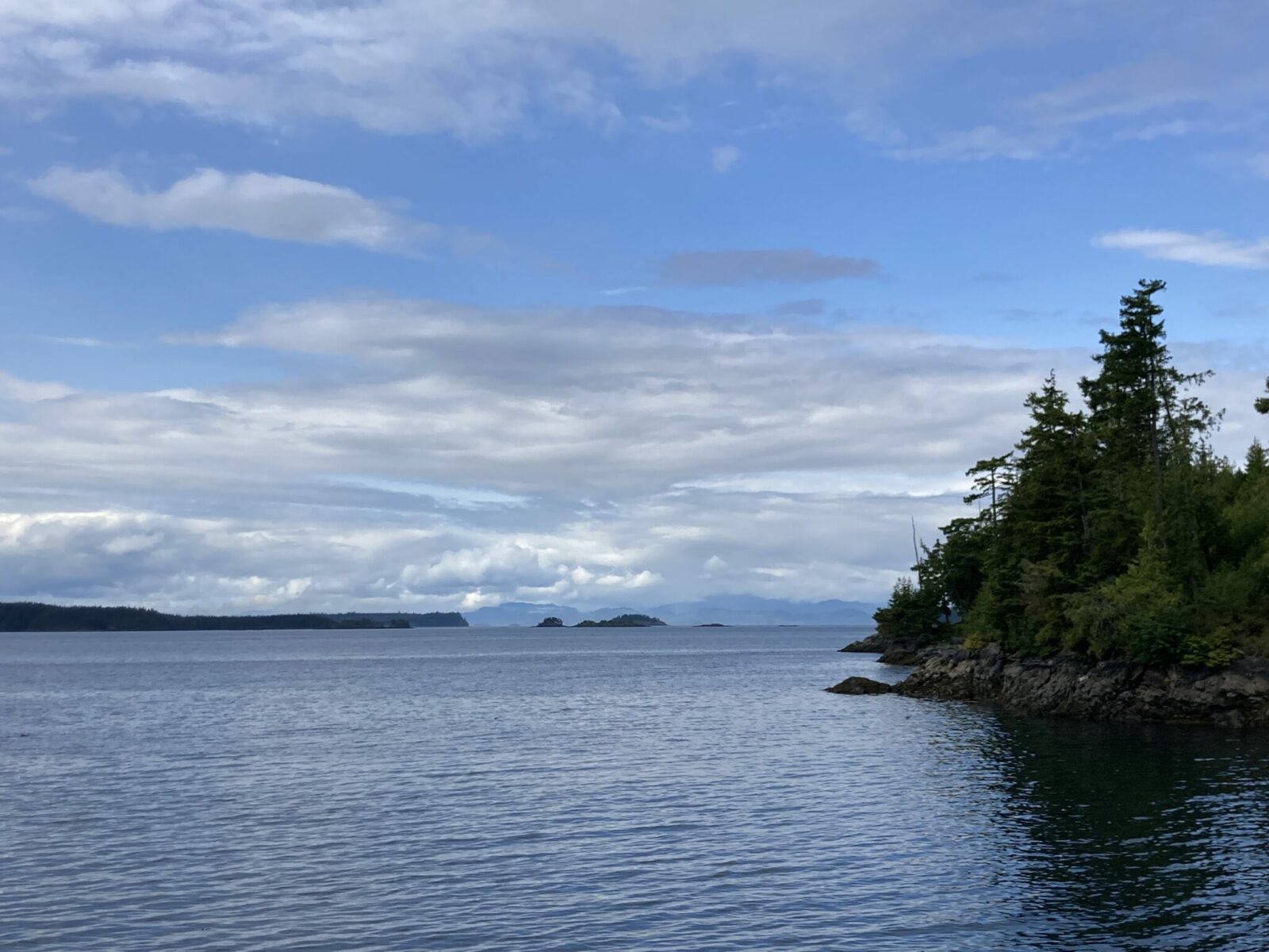 The entrance to Telegraph Cove, an inlet with rocky land and forest above and forested islands and mountains in the distance