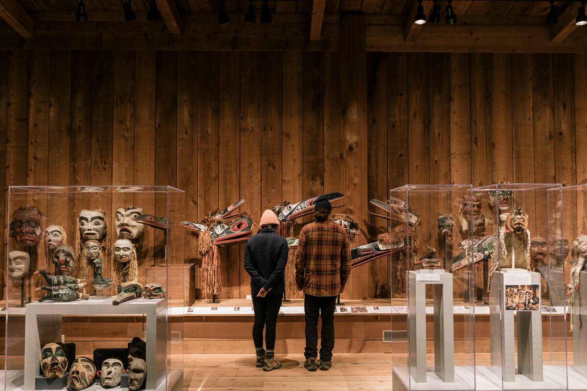 Two visitors in a museum looking at a display of First Nations masks.