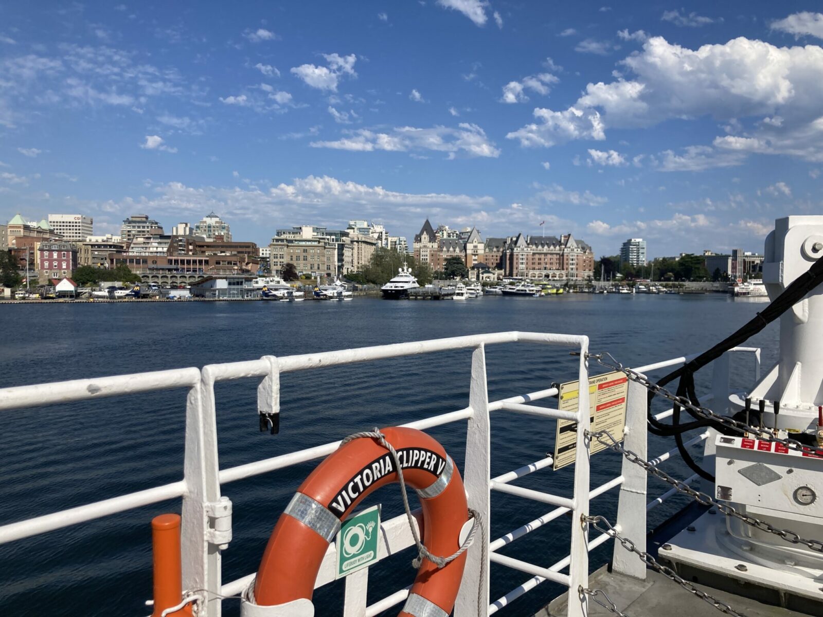 The deck of a ship in a busy harbor with lots of buildings and boats going by