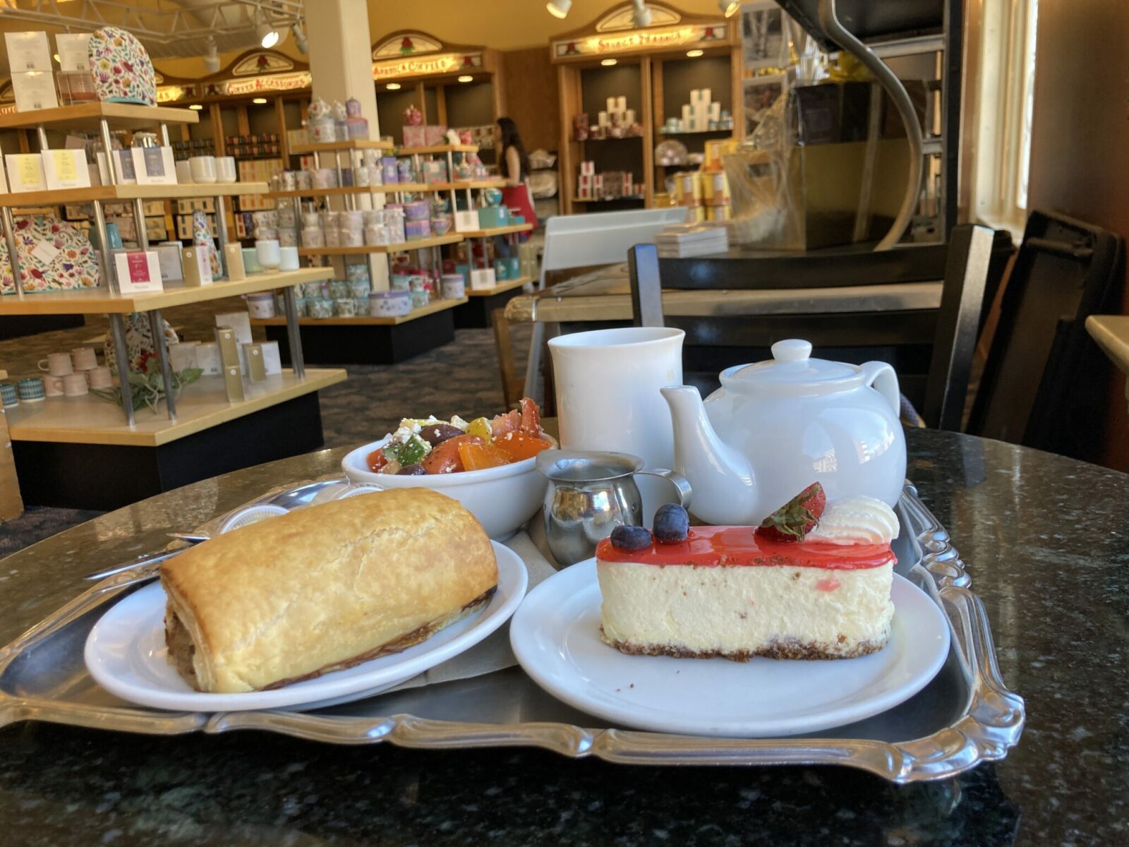 a silver tray with a white tea pot, a piece of cheesecake and a sausage roll at Murchie's in Victoria